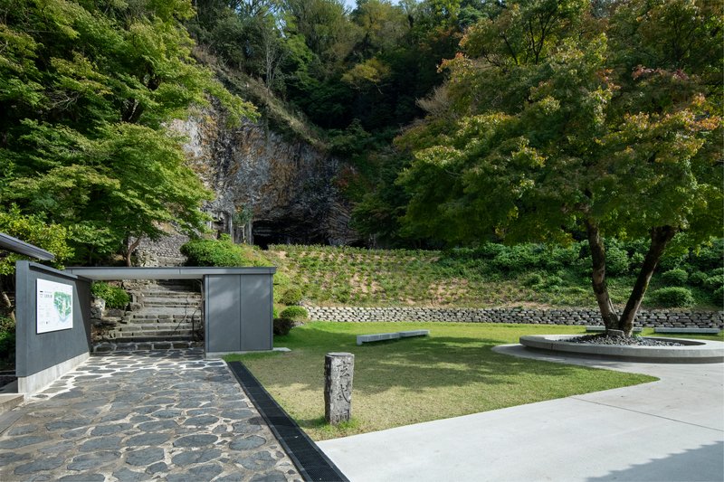 Entry pavilion with dark metal cladding and timber screen facing a lawn and stone retaining walls