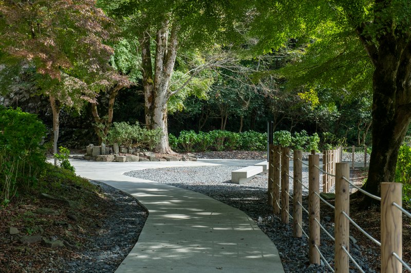 Curving concrete pathway with timber post railings winding through gravel beds and wooded plantings