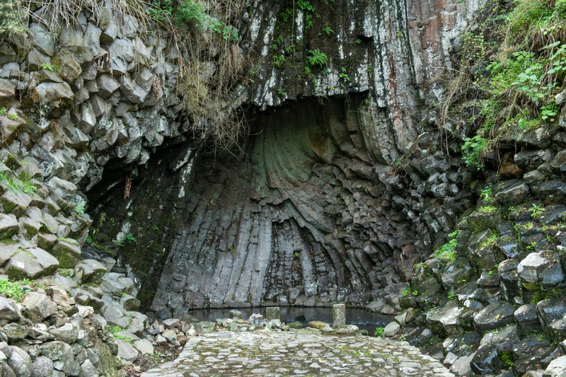 Stone grotto entrance with hexagonal basalt columns framing a vaulted ceiling and cobblestone floor