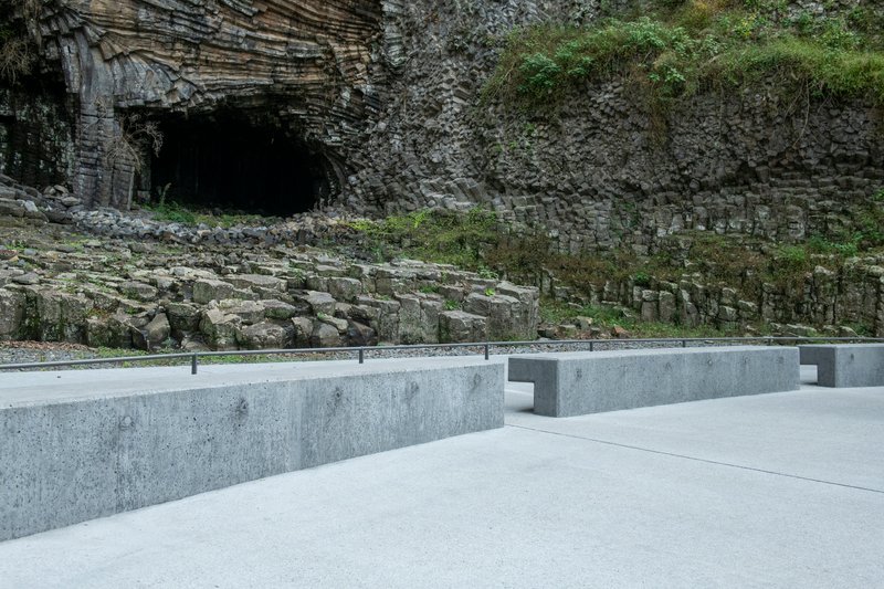 Low concrete wall with integrated bench seating and metal railing facing the columnar rock formation