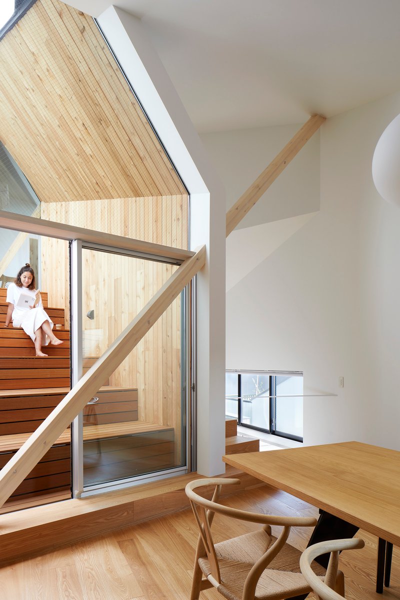 Double-height living space with timber stair and occupant seated on steps beside glazed partition