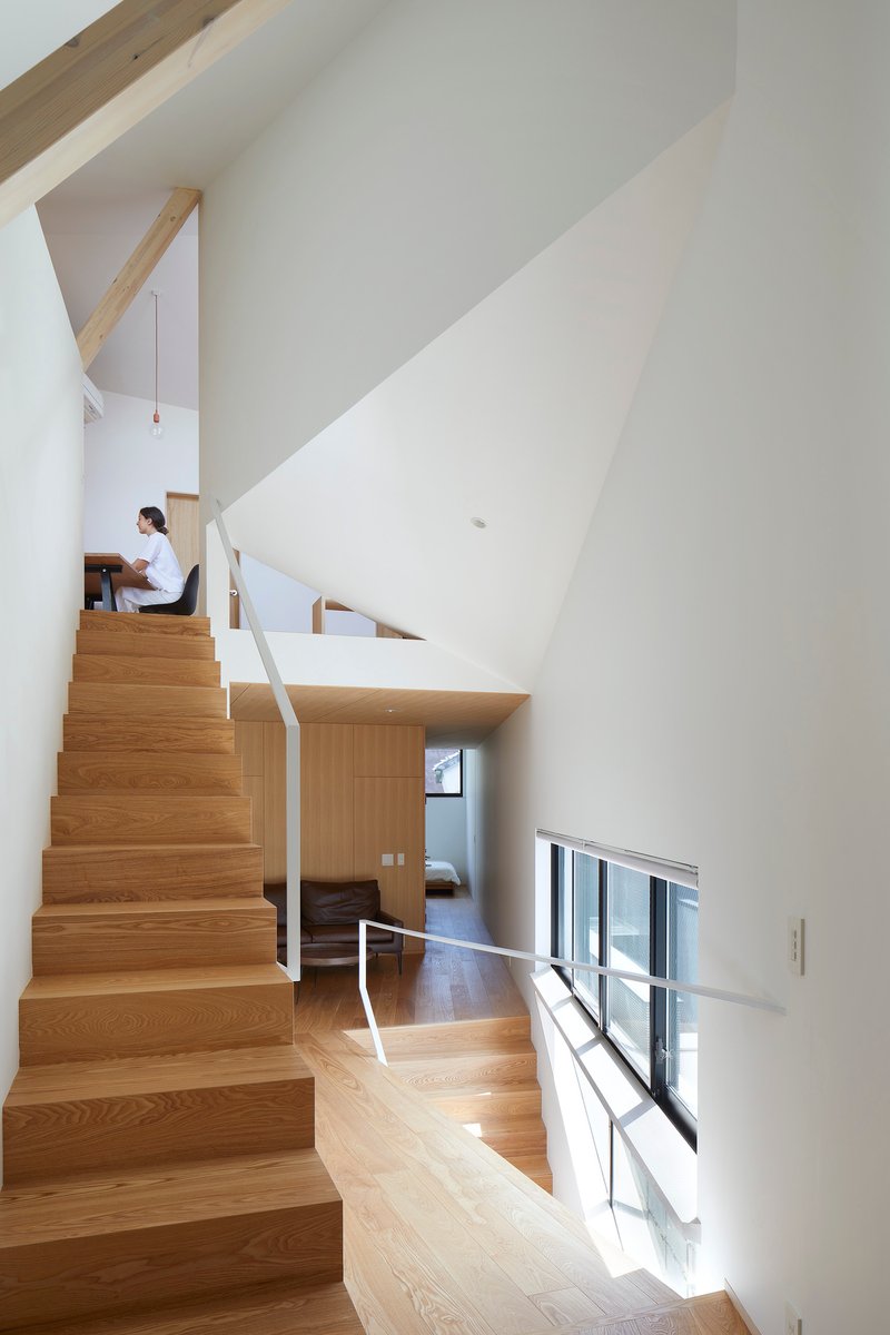 Multi-level interior with timber staircase and white metal railings where a person sits on an upper landing