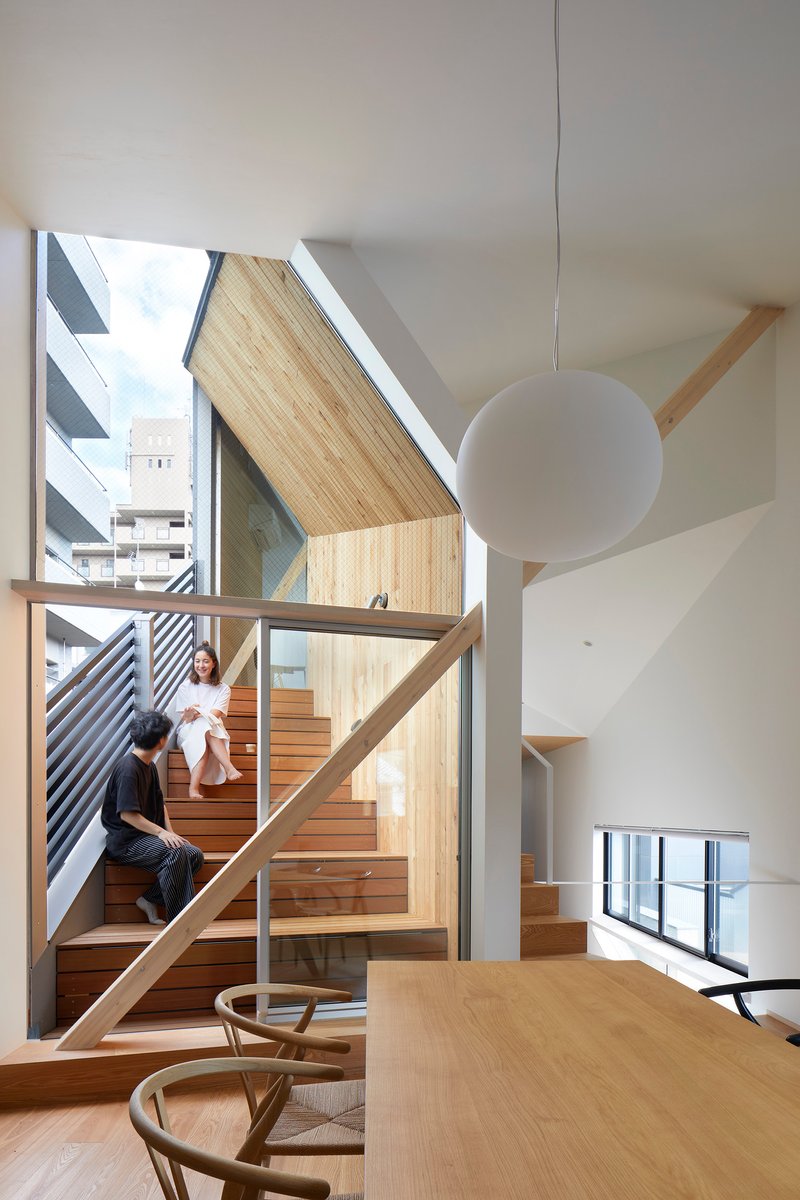 Double-height stairwell with exposed timber beams and large glazed wall overlooking neighboring rooftops