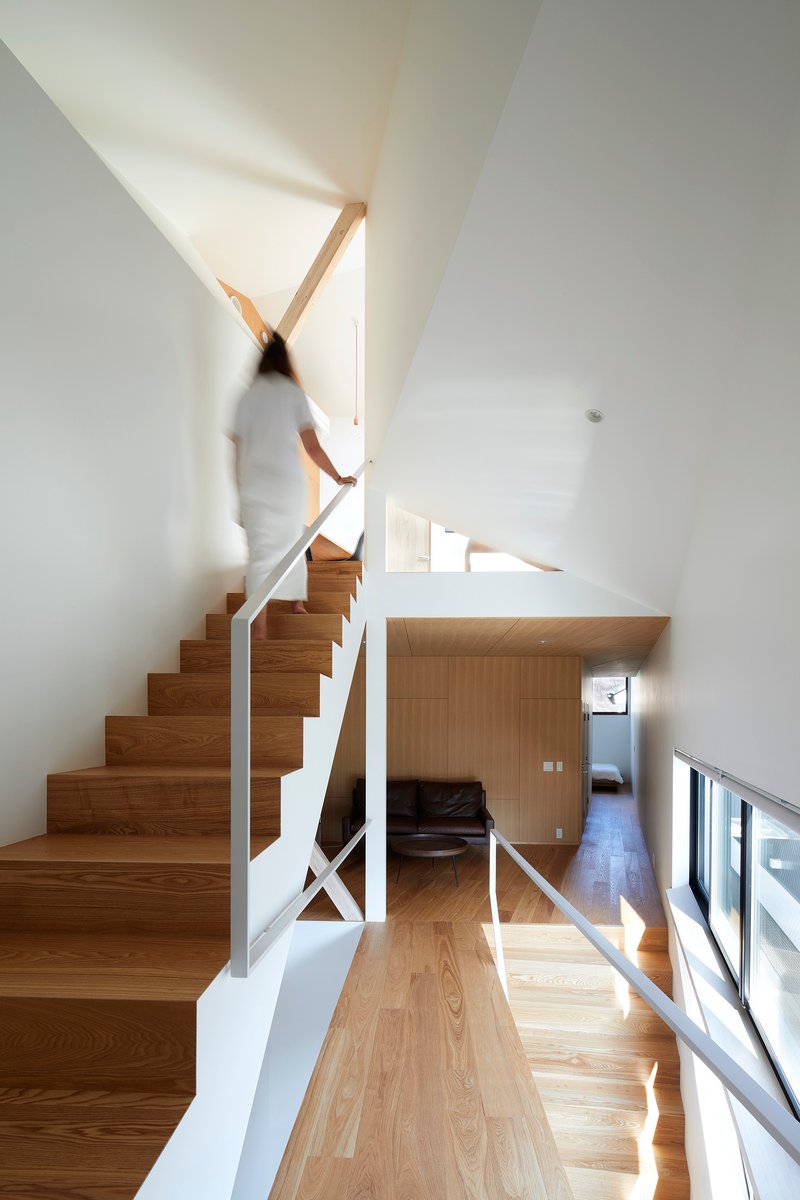 Timber staircase with white metal railing as a figure ascends toward a skylight above