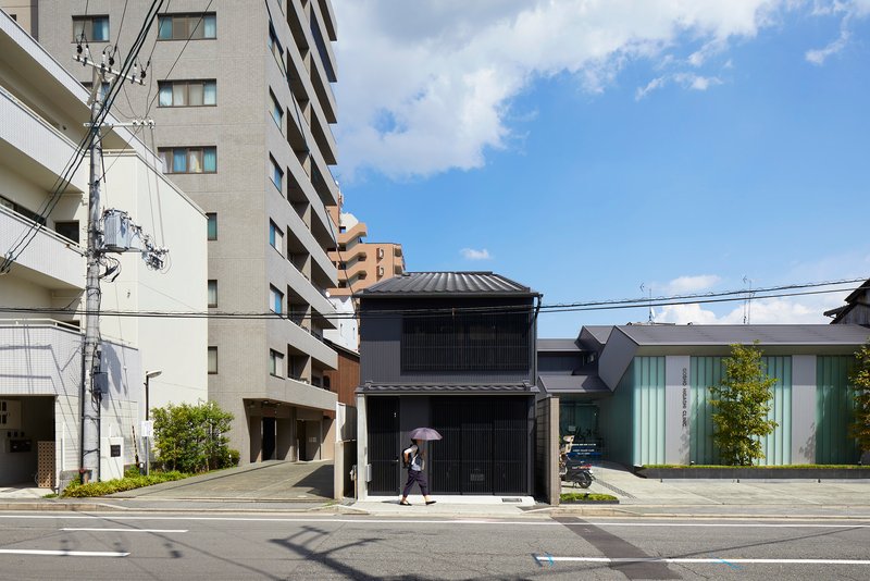 Black slatted facade of a two-storey house nestled between mid-rise apartment buildings under blue sky