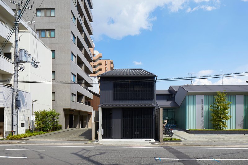 Street view of the vertical slatted black timber facade with tiled roof under scattered clouds
