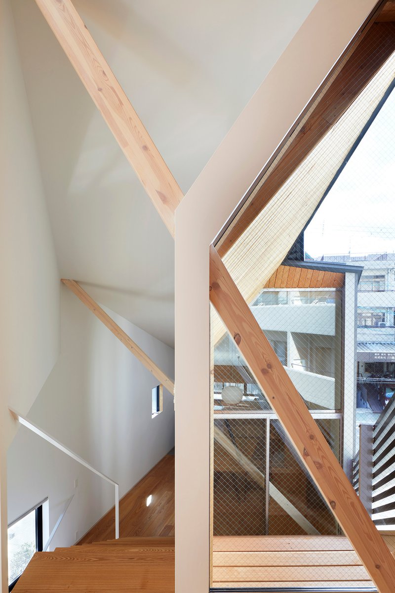Interior stairwell with exposed timber beams framing glazed openings that reveal neighboring buildings