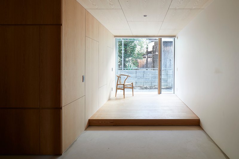 Corridor with pale timber storage wall leading to glazed doors opening onto a mesh-screened courtyard