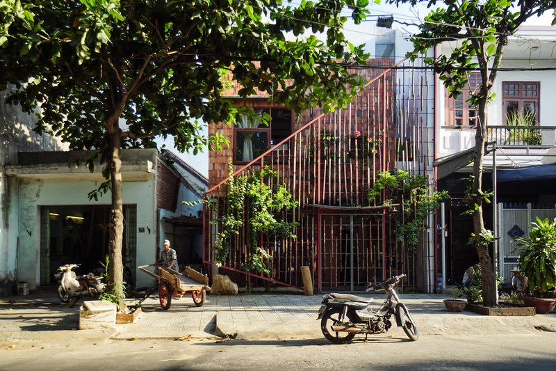 Street view of the vertical metal slat facade with planted vegetation framed by leafy street trees