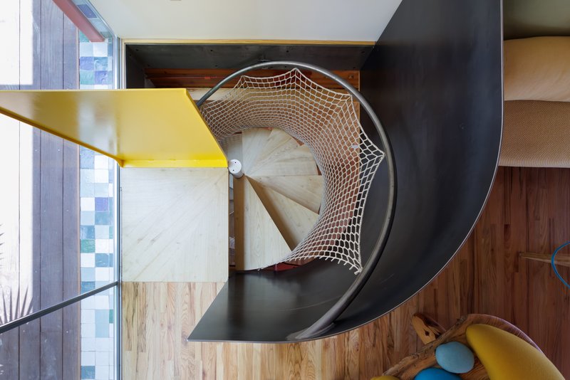 Overhead view of a curved staircase with rope netting balustrade and yellow steel handrail
