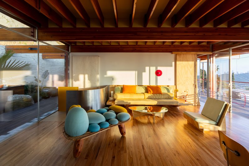 Open-plan living room with exposed timber beam ceiling and full-height glazing to courtyard in afternoon light