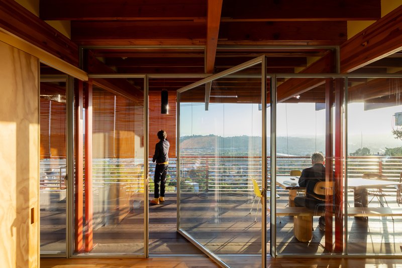 Floor-to-ceiling glass doors framing two figures on exterior deck with distant hills visible at dusk