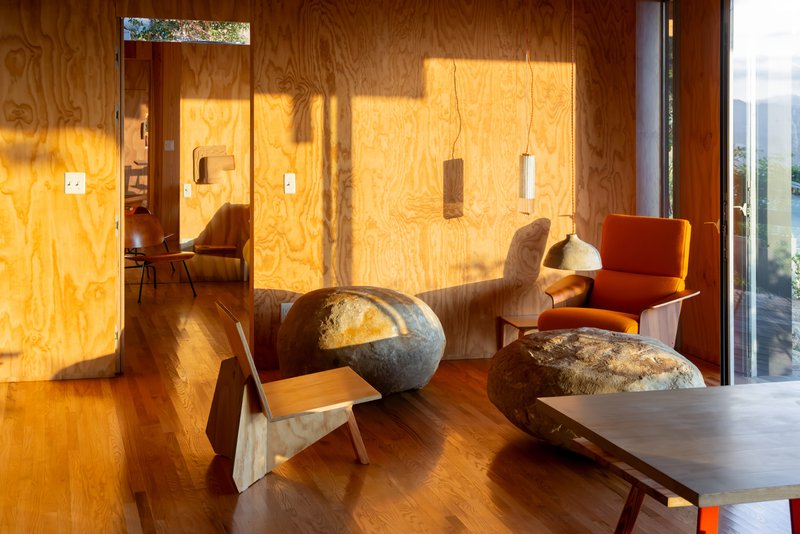 Living room with plywood walls catching afternoon sunlight and a sculptural stone coffee table on wood flooring