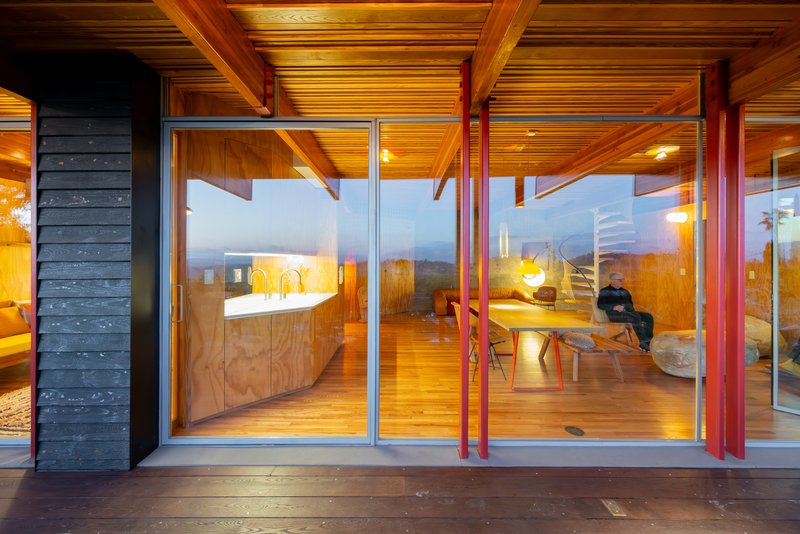 Glass facade framing the kitchen and dining area viewed from the exterior deck at dusk