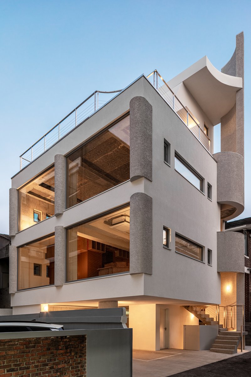 White rendered facade with cylindrical columns and exposed timber ceilings illuminated at dusk