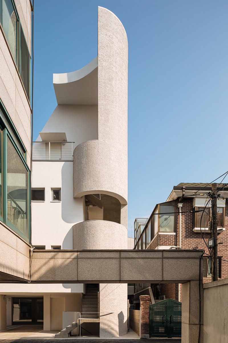 Curved cylindrical tower element with textured plaster finish rising above a horizontal concrete bridge