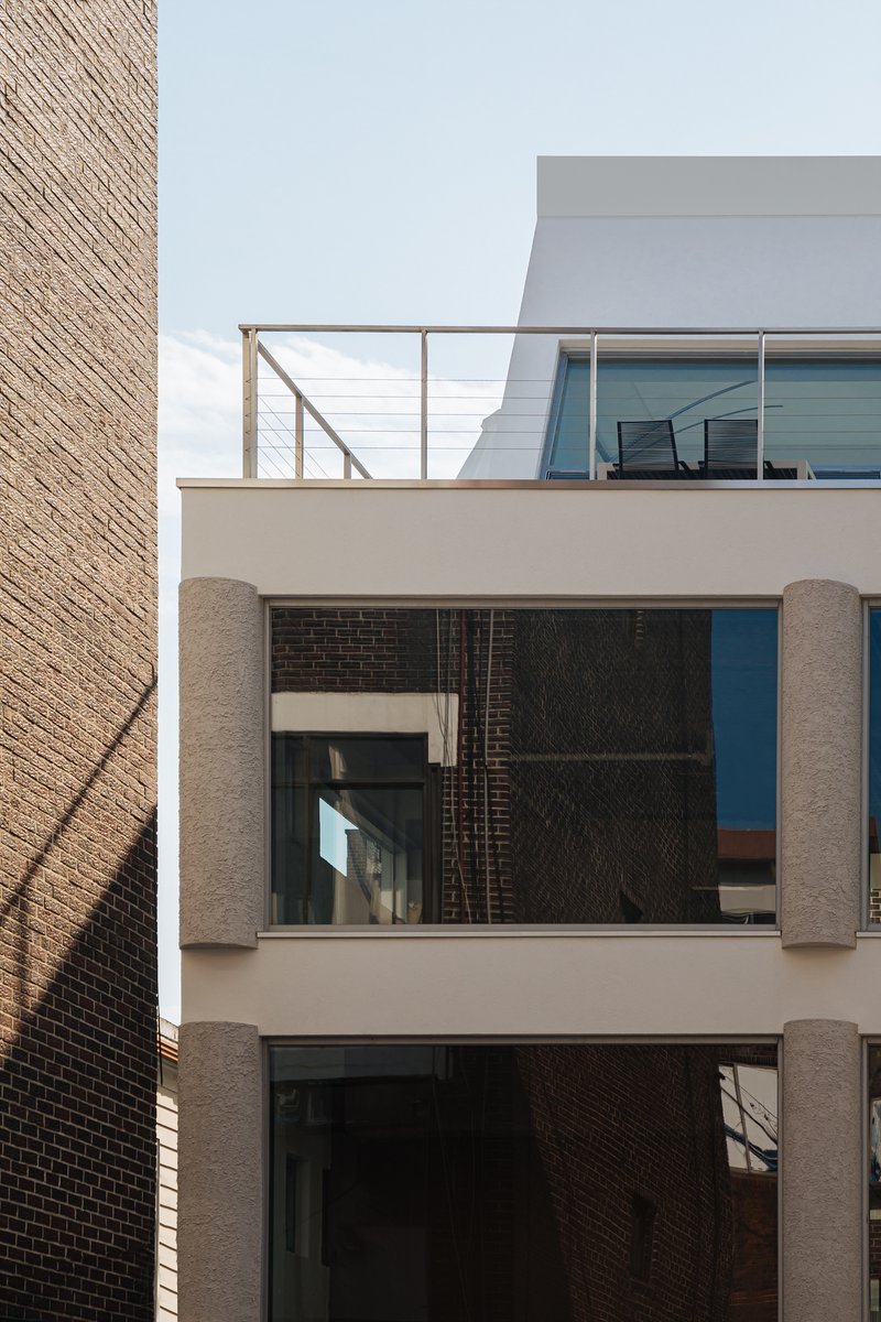 Street facade showing cylindrical columns framing recessed glazing beside a brick party wall