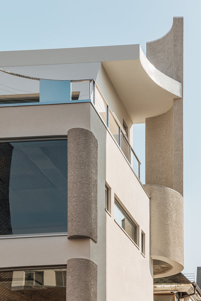 Textured cylindrical columns and curved balconies framing horizontal window openings under a clear sky