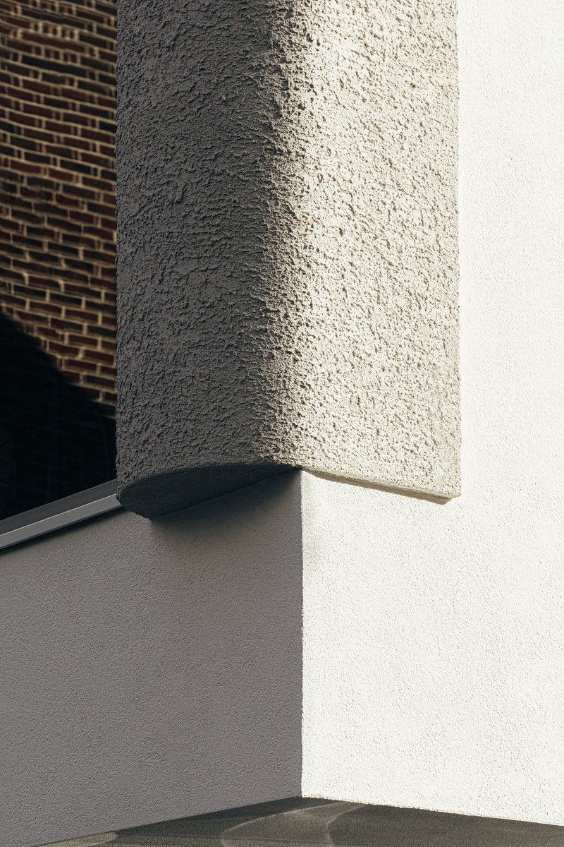 Close-up of textured stucco corner pillar with angled sunlight against adjacent brick wall