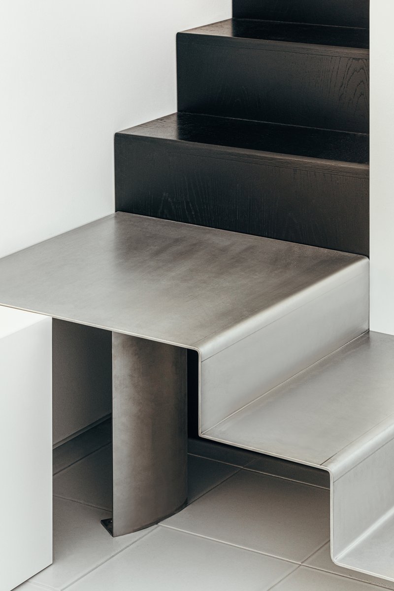 Detail of folded metal stair treads meeting black timber risers in a white interior