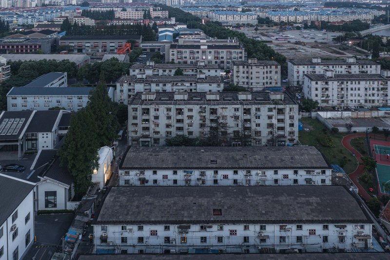 Drone view of the illuminated house nestled between residential blocks and a sports court at twilight