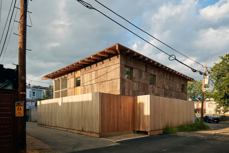 Street corner view of the two-story volume with exposed rafter tails and vertically clad timber fence below
