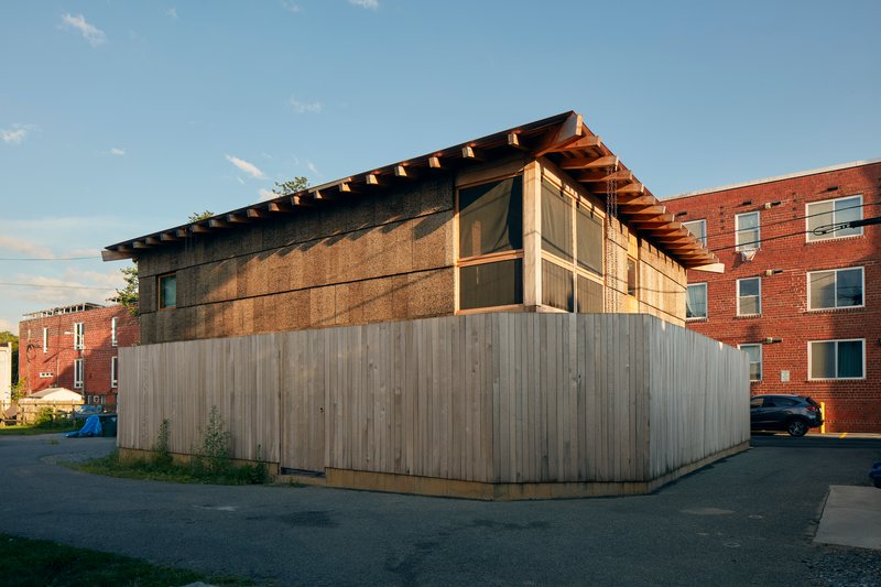 Facade showing upper compressed strawbale panels above vertical timber cladding at dusk
