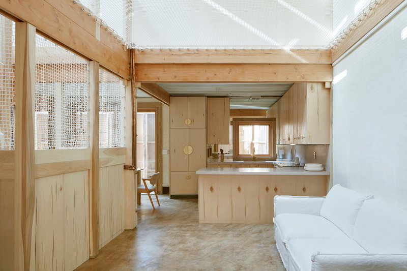 View through timber-framed mesh doors toward kitchen under a translucent skylight