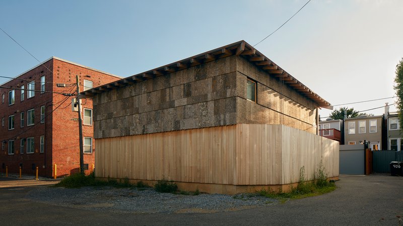 Corner view of the timber-clad base and cast-stone upper facade with exposed rafter ends at dusk