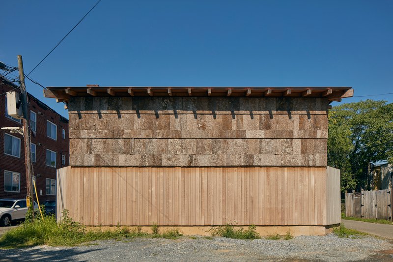 Street elevation showing the layered facade with vertical timber cladding below cast-stone panels and deep eaves