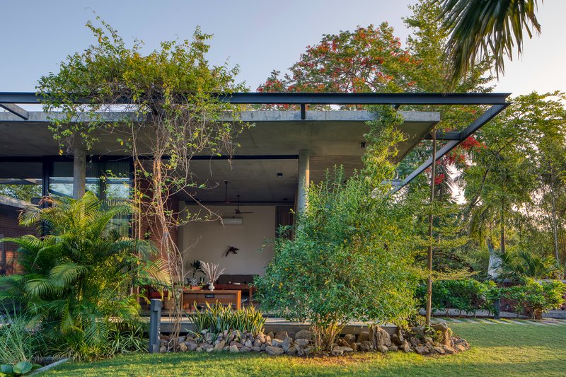 Covered outdoor pavilion with steel frame and concrete soffit surrounded by palm trees and tropical planting