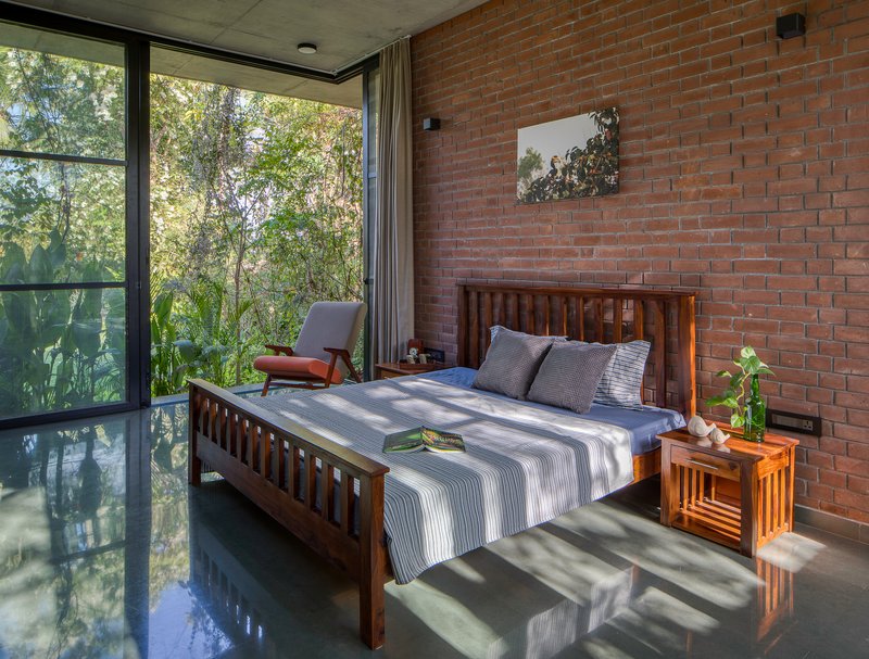 Bedroom with exposed brick wall and floor-to-ceiling glass overlooking garden with filtered morning light