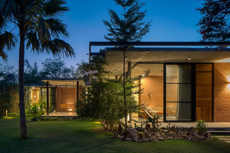 Illuminated glass pavilions with brick and timber facades set in a garden at twilight