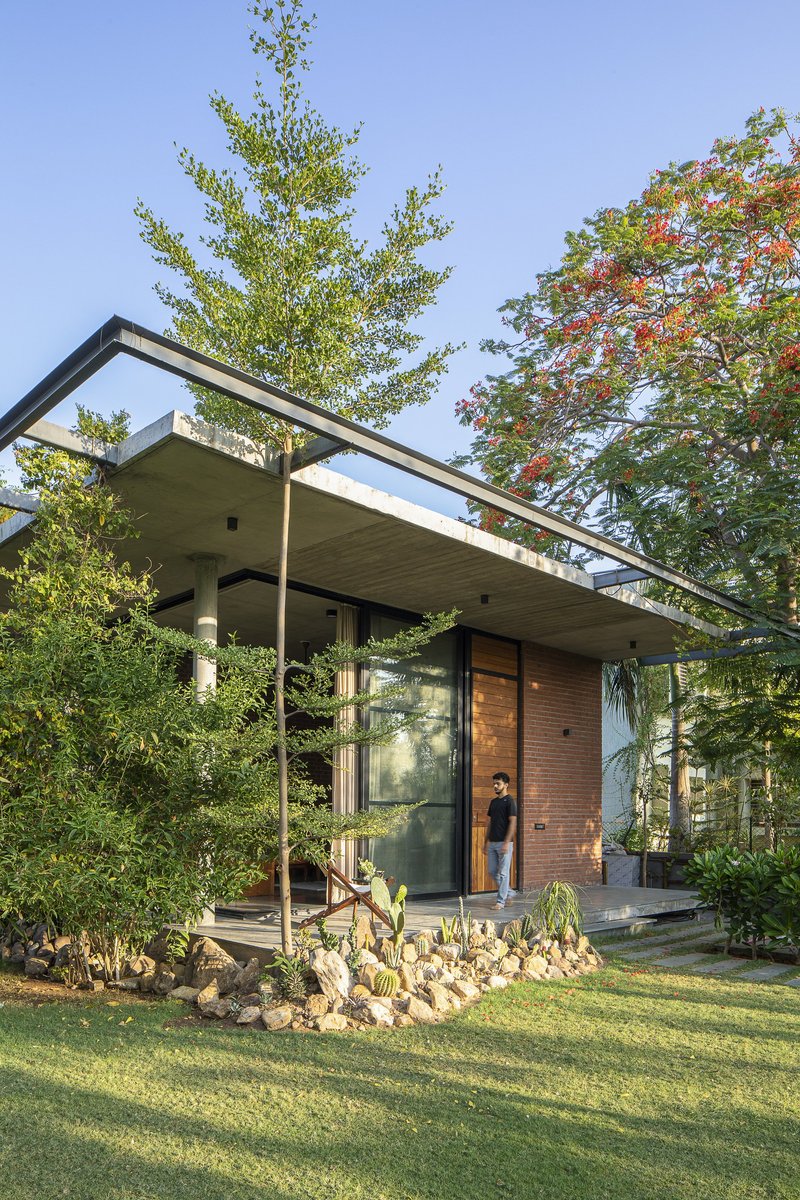 Front elevation showing the steel-framed roof canopy with a figure standing at the timber-clad entrance