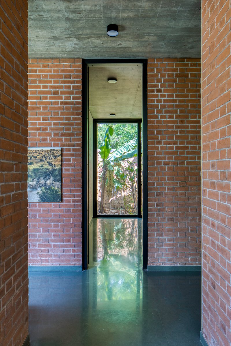 Narrow corridor with buff brick walls flanking a tall vertical window framing vegetation outside
