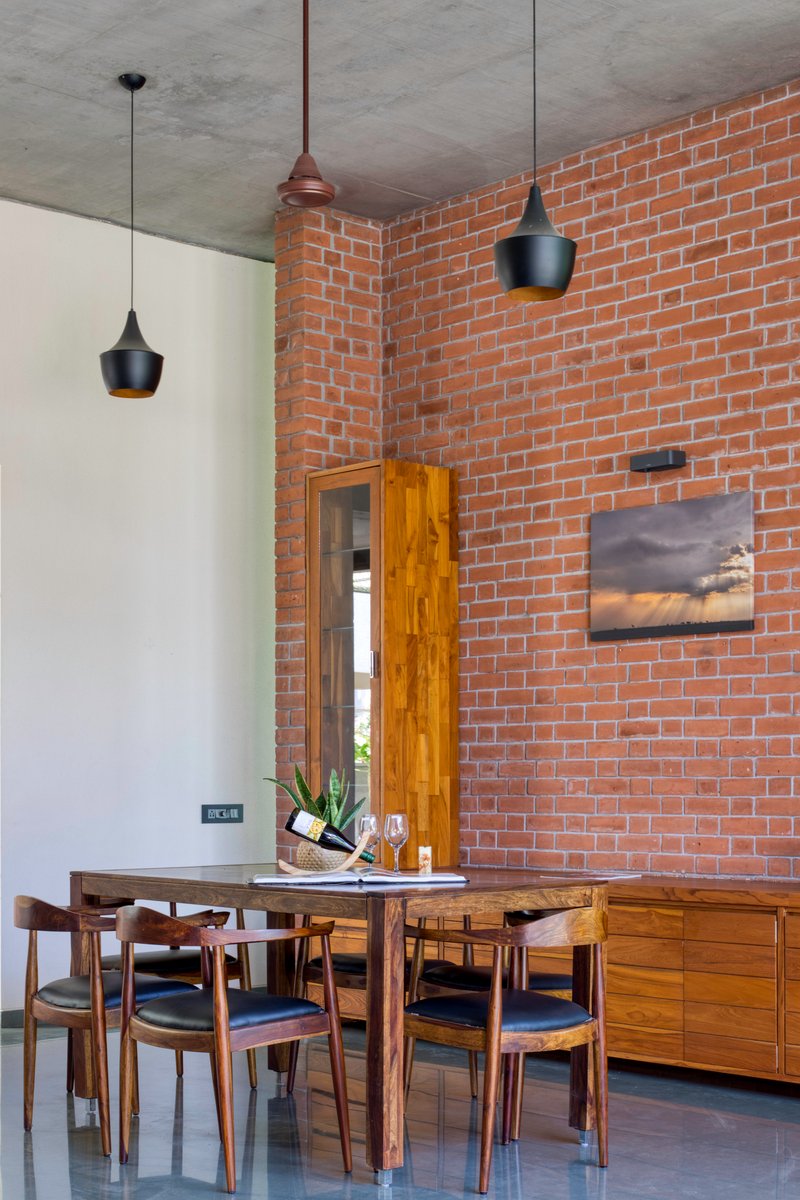 Dining area with exposed brick wall, concrete ceiling, black pendant lights, and timber furniture