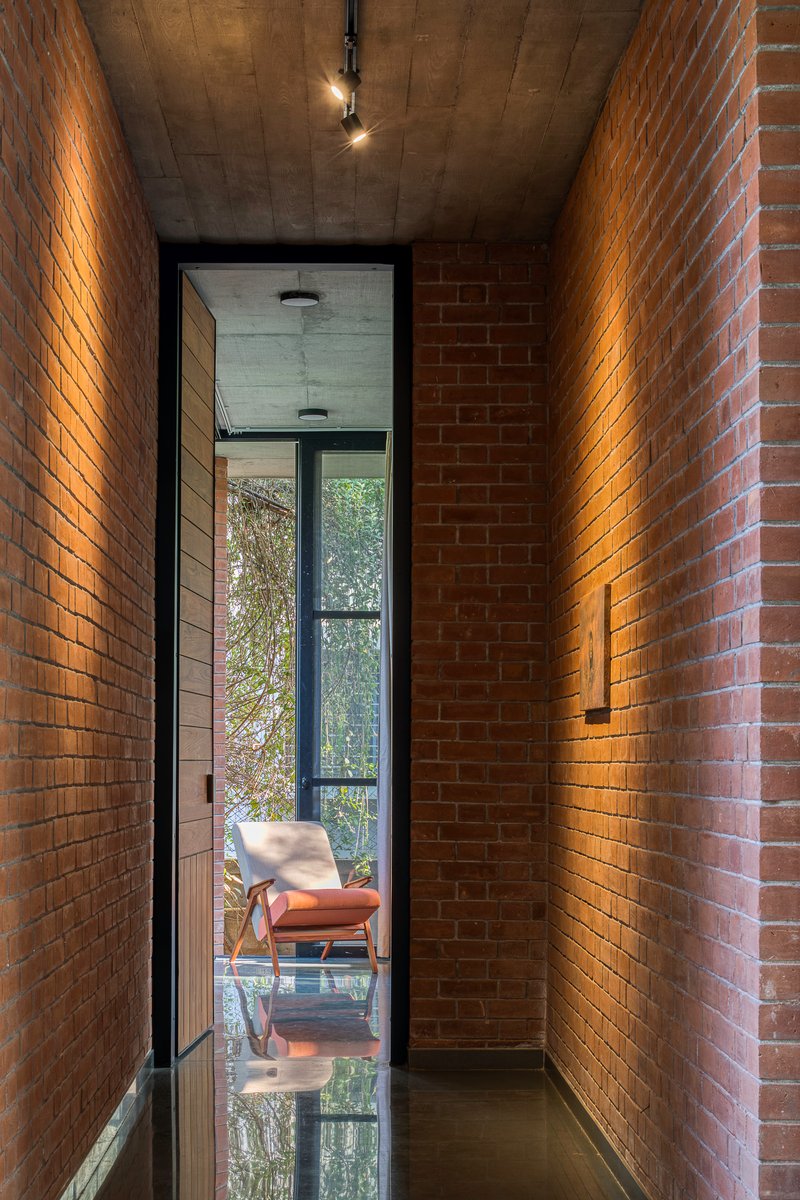 Narrow brick corridor with uplighting leading to a glazed threshold and concrete ceiling