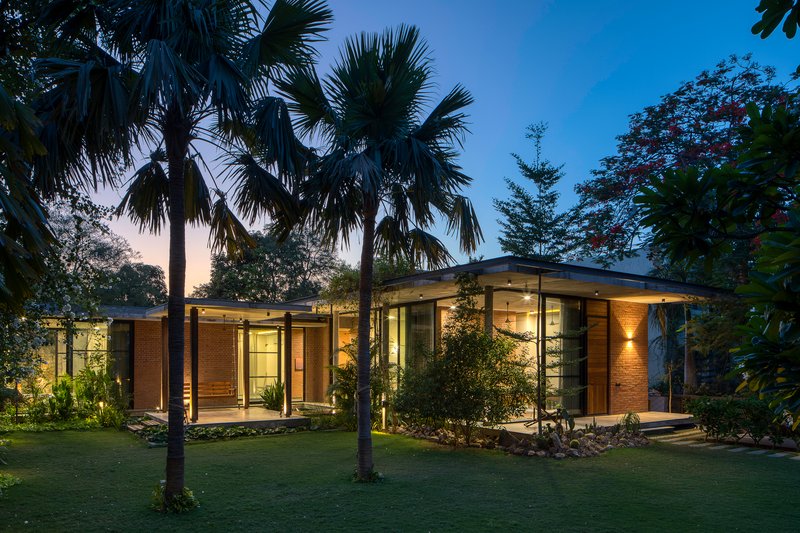 View of the illuminated brick and glass pavilion through palm trees at dusk