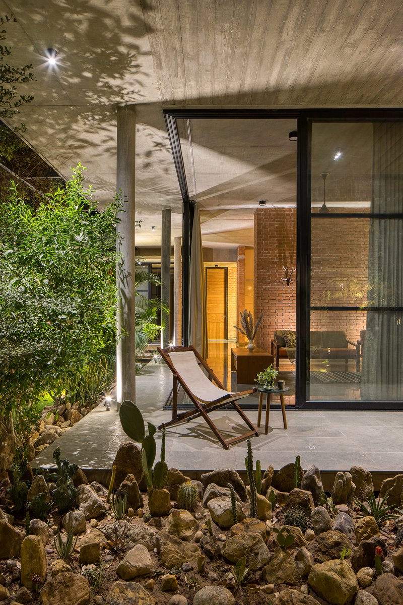 Courtyard terrace with planted cacti bed and lounge chair under concrete soffit at dusk