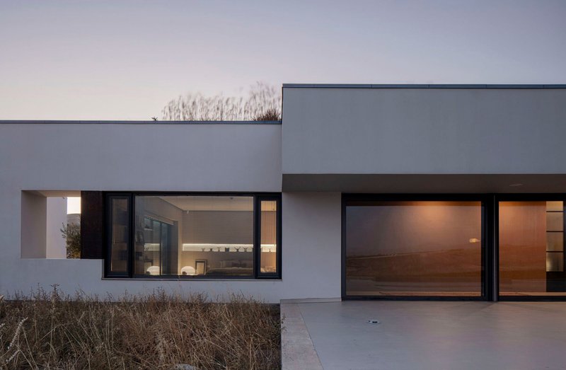 Illuminated interior visible through black-framed glazing at dusk with parched grasses in foreground