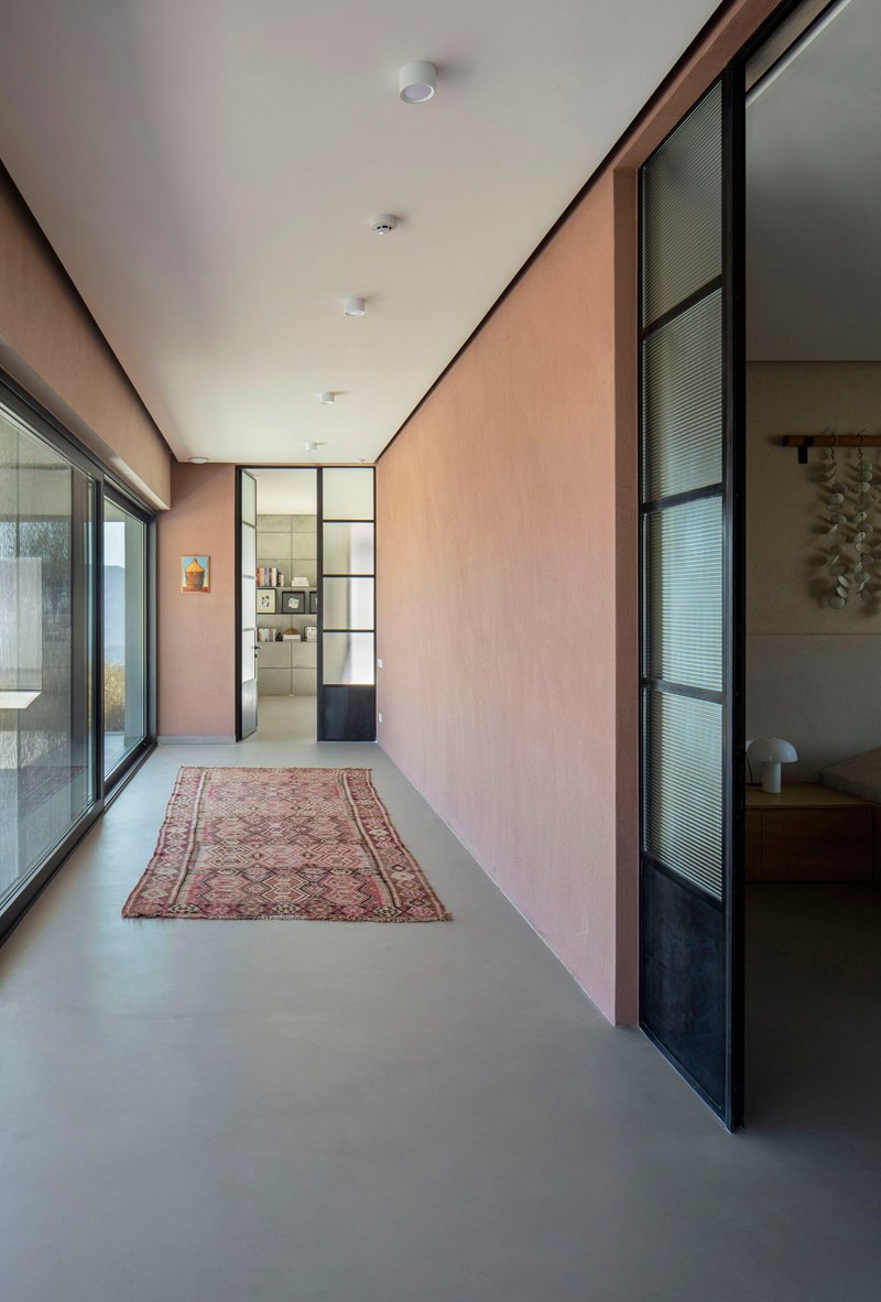 Corridor with pale plaster walls, steel-framed glass partitions, and a vintage rug on polished concrete flooring