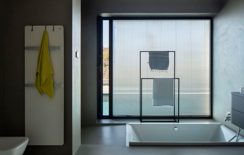 Bathroom with recessed tub beside a window fitted with translucent pleated blinds and a towel rack