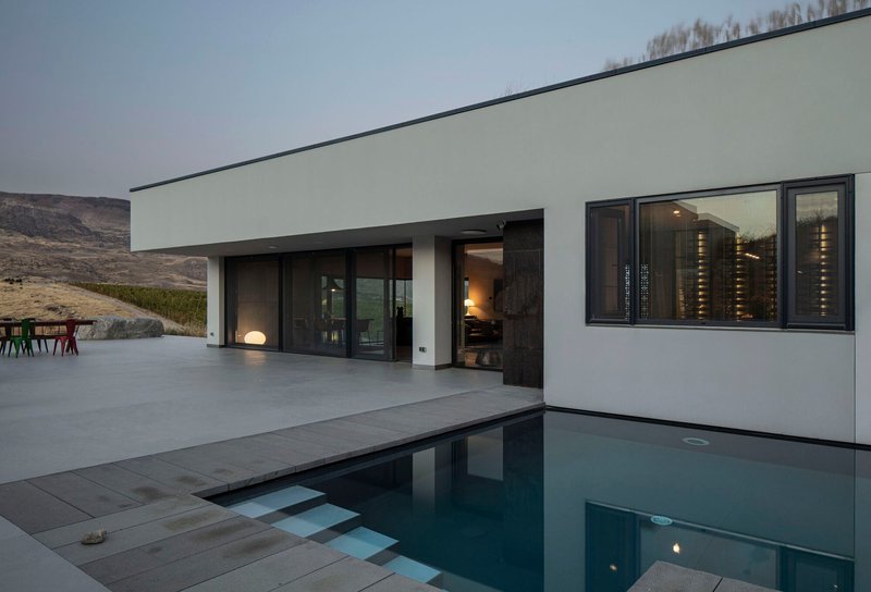 Pool deck at dusk with still water reflecting the interior lights through sliding glass doors