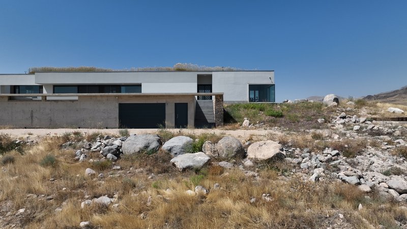 White horizontal volume with terrace roof set among rocky desert terrain under clear blue sky