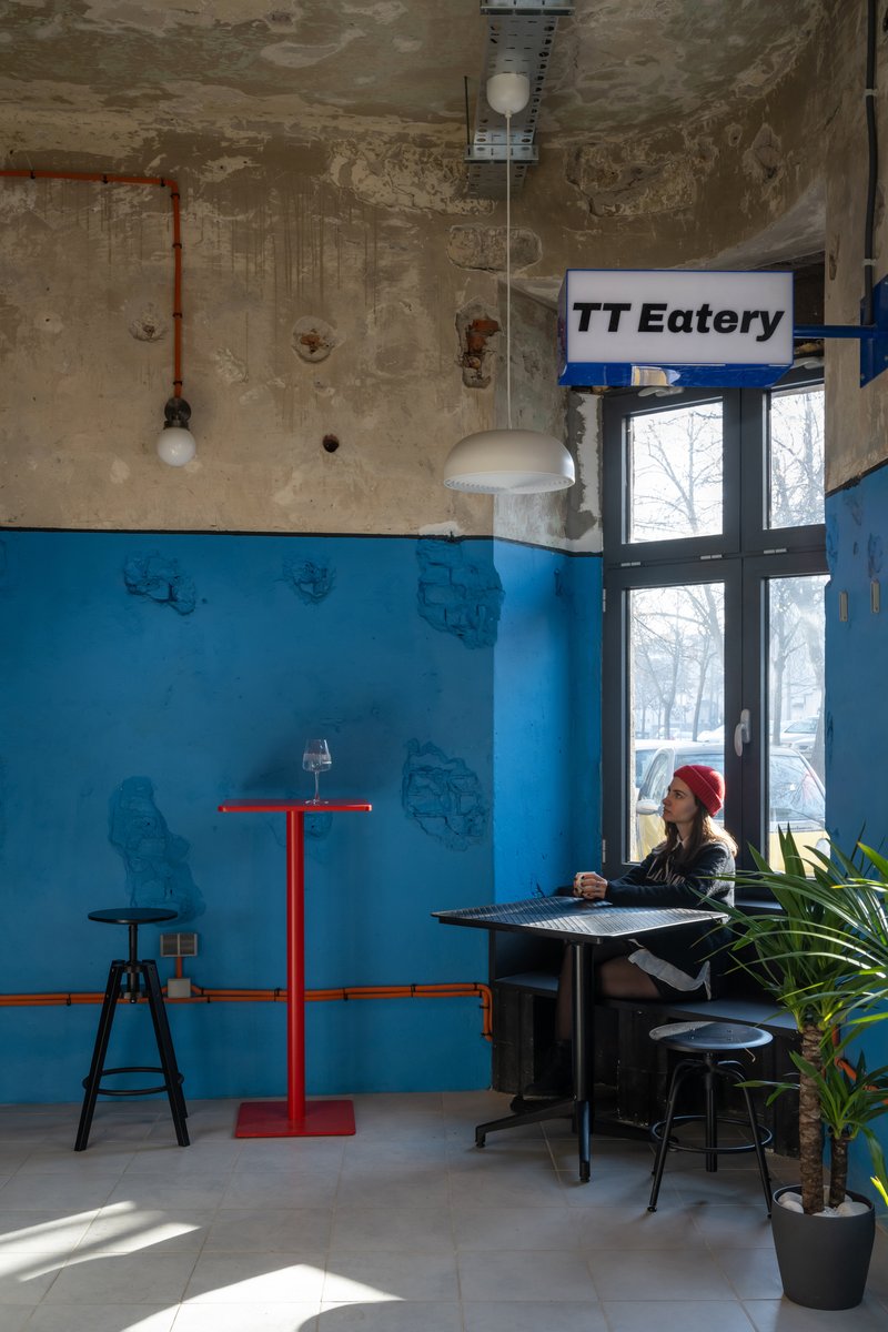 Seated figure at a table beneath weathered concrete ceiling with exposed conduit and pendant lighting