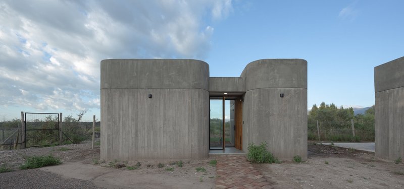 Cylindrical concrete volumes flanking a recessed glass entry in a sparse desert setting