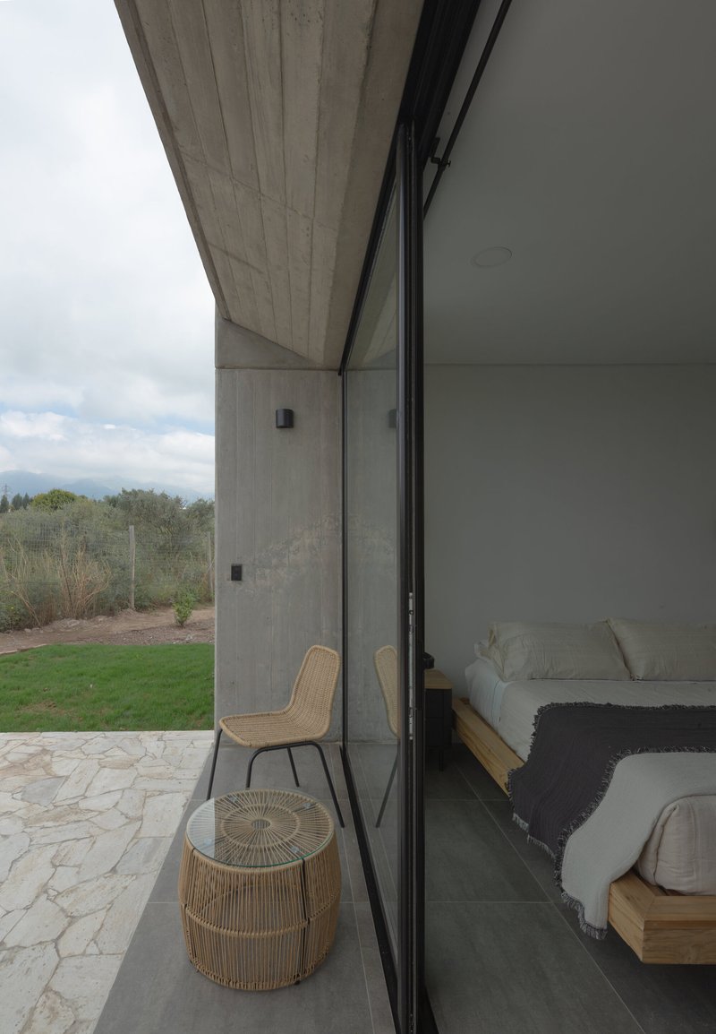 Bedroom terrace with rattan furniture framed by sliding glass and a board-formed concrete soffit