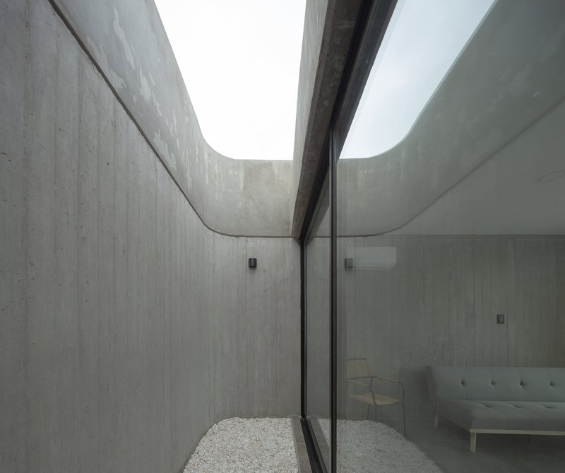 Interior courtyard view with curved concrete walls and a narrow skylight above gravel floor