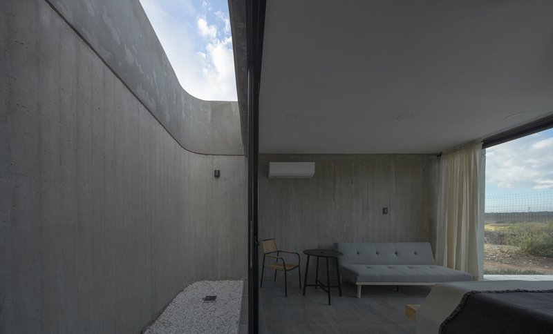 Bedroom interior opening to a private courtyard through floor-to-ceiling glass under an overcast sky