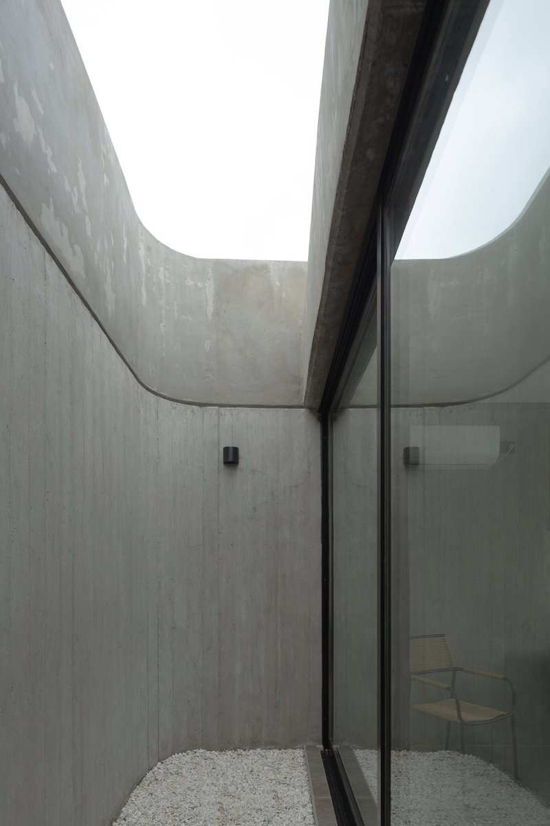 Interior courtyard with board-formed concrete walls and a curving skylight opening above gravel flooring